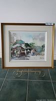 Framed watercolor painting showing whole scene with gold frame and easel