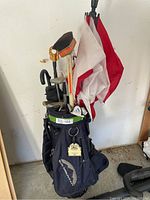 Overall view of the Sun Mountain navy blue golf bag with golf accessories inside including umbrellas, ball retrievers, and other items inside the garage.