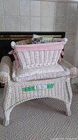 White wicker basket with wooden handles and pink gingham fabric lining placed on top of the wicker bench with cushion.