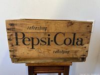 Side view of the wooden Pepsi-Cola crate showing large black 'Pepsi-Cola' logo, smaller wording 'refreshing' and 'satisfying', natural wood with age marks
