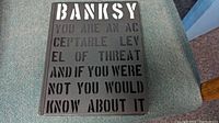 Front cover of the hardcover art book showing embossed stencil text reading 'BANKSY YOU ARE AN ACCEPTABLE LEVEL OF THREAT AND IF YOU WERE NOT YOU WOULD KNOW ABOUT IT'.