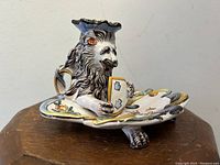 Front right three-quarter view of lion candle holder showing lion face, shield motif and scalloped base