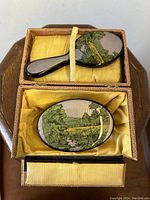 Top-down view of the set in the open lined box showing brush and mirror with scenic lacquered backs and yellow satin lining
