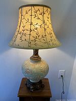 View of the lamp lit, showing warm glow through fabric lampshade with leaf pattern