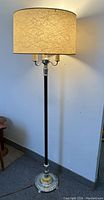 Full view of the Art Deco standing floor lamp, showing the tall slender black stem, silver decorative base, and parchment lampshade.