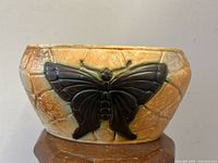 Front view of oval vase with prominent dark butterfly relief on textured crackle glaze background in warm earth tones.