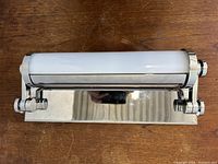 Front view of chrome wall light fixture showing tubular white glass shade and chrome mounting plate.