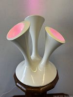 Front view of white Boob "BOOM" table lamp on wooden stool with pods illuminated pink.