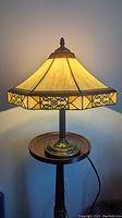 Lamp turned on showing warm glow from iridescent stained glass shade with decorative metal filigree