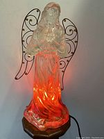 Front view of illuminated acrylic Christmas angel statue glowing red from internal light showing translucent dress and metal wings.