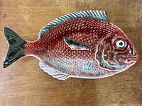 Top view photo of the red majolica fish platter showing detailed scales, fins, and eye, on a wooden surface.