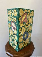 Side view showing raised yellow leaves with purple and blue bellflower patterns on green faience pottery.