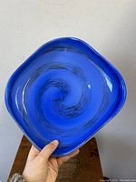 Square-shaped azure blue Murano art glass bowl with black swirl, held to show full front view and shape.