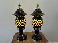 Pair of black Japanese pagoda style table lamps with lattice open orb section and gold finials on top shown lit.