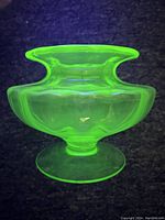 Front view under UV light showing glowing bright green uranium glass vase with ribbed body and flared top.