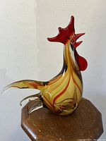 Front side view of the amber and red Murano glass rooster sculpture on wooden stand.