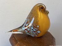 Side view of amber and speckled art glass bird sculpture on a wooden surface.