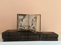 Six hardcover antique books with dark covers and gold decorative spines, one opened to a fold-out black and white illustrated title page saying "Journeys Through Bookland."
