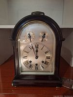 Front view of antique mantel clock with arched wooden case, Roman numeral face, and two smaller dials labeled Chime and Tent.