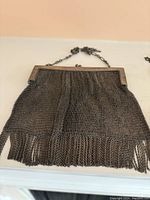 Large silver-tone mesh purse with fringed bottom and chain strap, lying flat.