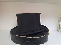 Black silk top hat displayed on original round box with edge wear.