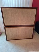 Pair of Bifrons speakers stacked vertically showing beige woven fabric covers and rectangular wooden frames