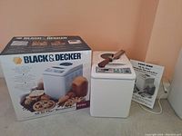 Photo showing the Black & Decker bread maker unit, original box and user manual, serrated knife on top of the bread maker.