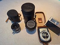 Full layout showing two camera lenses with cases, Solan Lunasix light meter, small leather case, and Braun F25 speedlight flash.