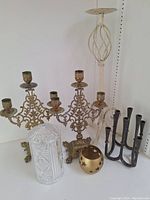 Photo showing all candle holders arranged together including brass candelabras, crystal cylinder cover, black menorah-style holder and small golden tealight holder
