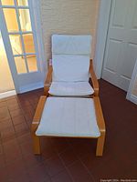 Full view of the IKEA wooden frame chair with white fabric cushions and matching ottoman on tiled floor.