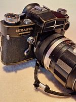 Close-up image of Miranda camera body and attached telephoto lens showing brand name, lens markings, and wrist strap.