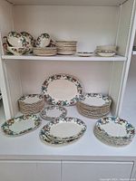 Full display of the Royal Cauldon 'Victoria' china set arranged on two shelves, showing large number of plates, bowls, and soup cups with floral pattern and gold edging.