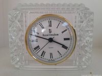 Photo showing the Royal Doulton crystal clock with a clear square cut crystal body and classic clock face with black Roman numerals and gold trim.