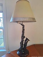 Front view of saxophone lamp showing beige lampshade with musical notes and saxophone base.