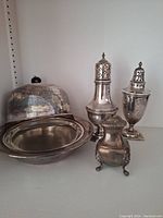 Overall view of silver plate butter dish, salt and pepper shakers, and small covered container. Shows tarnish and wear, needs cleaning.
