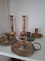 Full view of all six silver-plated candle holders arranged in two rows, showing variety in size and style with some tarnishing visible.