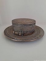 Front view of silver plated covered butter dish resembling a woven hat with buckle detail on base plate.
