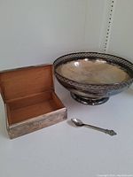Silver plated round footed dish with decorative rim, rectangular box with open lid showing wooden interior, and small spoon in front.