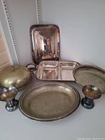 Overall view of silver plated serving pieces grouped together on shelf showing tarnished surfaces and item shapes