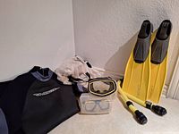 Full view of wetsuit, flippers, masks, snorkels, and mesh bags arranged on floor and against wall.