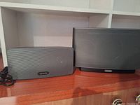 Two Sonos speakers side by side on wooden surface