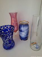 Four decorative vases displayed together showing various colors and styles including cobalt blue, pink, blue-white ceramic, and clear glass with objects inside