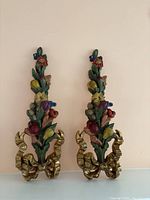 Pair of wood carvings with colorful flowers and gold bases against a pale background.