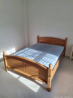 Solid wood double bed frame assembled with mattress on top in a well-lit room.