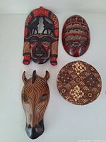 Top view of all items: three wooden masks and one round woven basket laid on a flat surface.