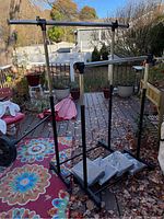 Two black metal adjustable rolling clothes racks on a deck outdoors. One rack shows some rust on the horizontal bar. Four large white or off-white fabric garment or quilt storage bags placed at base of racks.