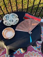 Top view of two Asian style bowls and the wooden fan with box on a black cloth.