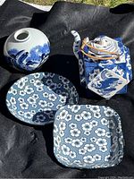 Photo showing all four items on black cloth: the vase, hexagonal dragon teapot, round and square floral plates.