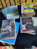 Books displayed on a small round black table outside with a railing and leaves in the background. Featuring a visible mix of titles including Donna Morrissey, Daniel J. Levitin, Sy Montgomery, and Terry Pratchett covers.