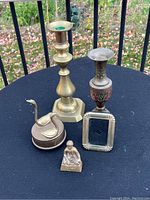 Photo of five items on table - brass candlestick, bronze vase, music box with swan, small picture frame, bronze musician figurine
